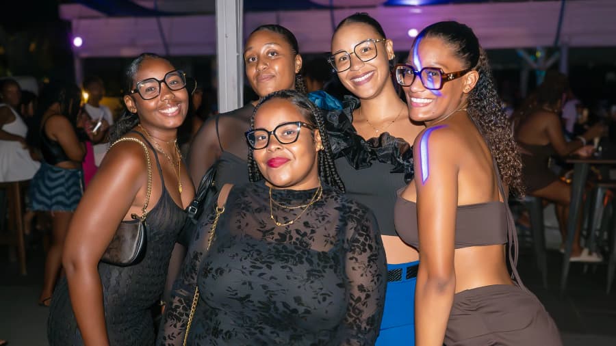 Cinq amies à lunettes posent ensemble sous des lumières violettes